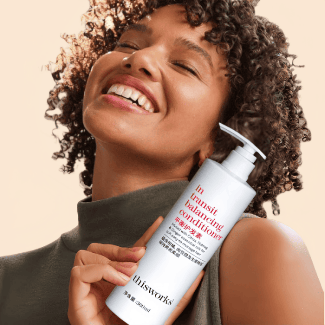 The lady holds the hotel conditioner in her hand, she smiles and squints her eyes, looking like she is enjoying it.