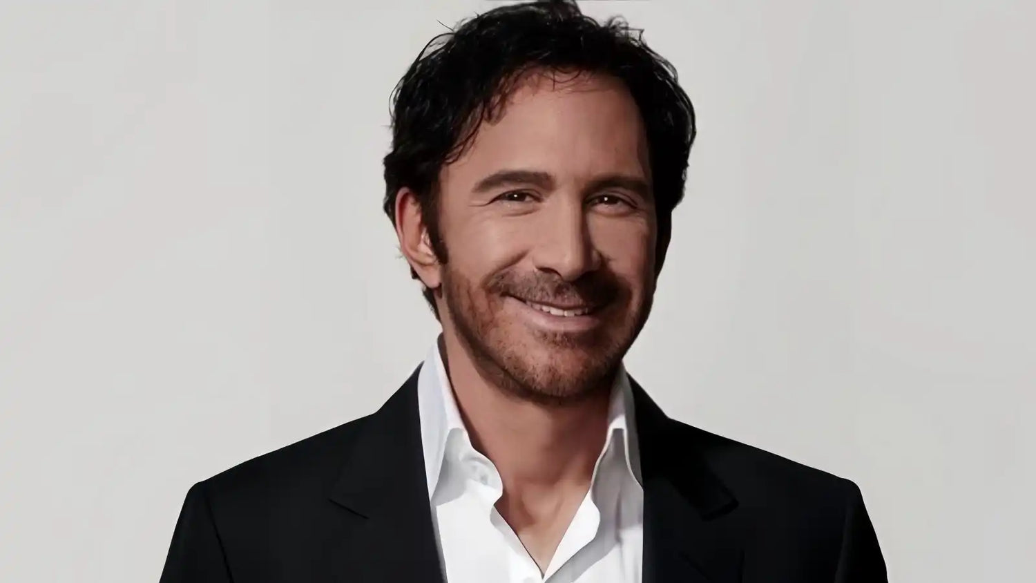 Gray background, Peter Thomas Roth white shirt with black suit, he smiles, very elegant